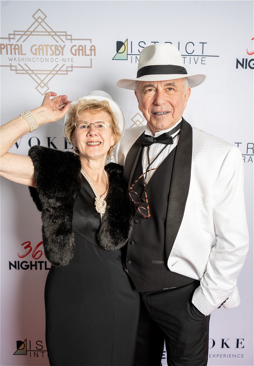 A couple in black and white Great Gatsby clothing pose in front of the Step & Repeat at the Capital Gatsby New Year's Eve DC Gala at HQO in Navy Yard. This event attracts people of all ages (21+ only).