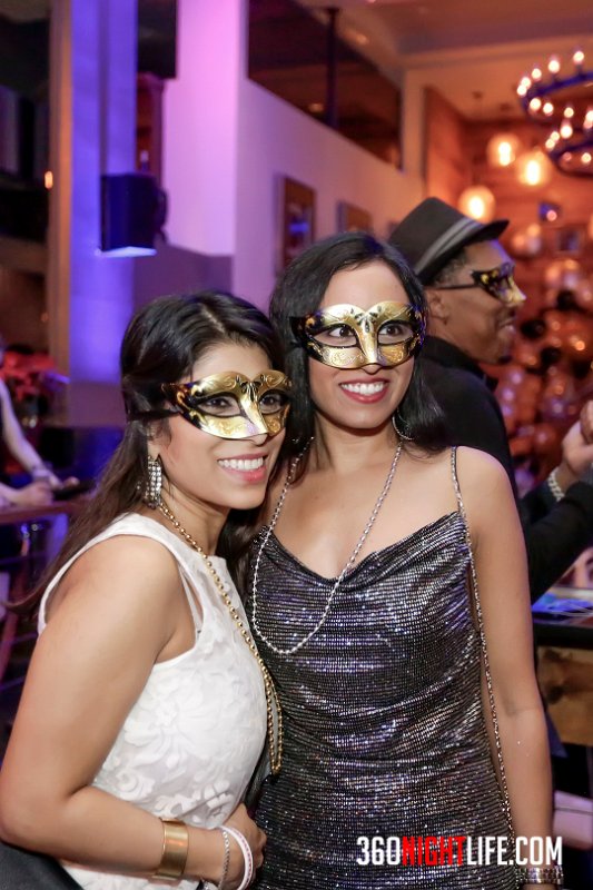 2 women in gold masquerade masks. The woman on the right is in a white dress with gold necklace (beads), the woman on the right is in a dark gray / silver dress with silver beads. These were given out by 360 Nightlife as party favors. This picture was taken at National New Year's Eve Masquerade Ball by 360 Nightlife in Washington, DC. The original website was https://www.360nightlife.com but we have revamped to https://www.360nigthlife.com. Please note: all rights reserved. These photos are sole copyright of 360 Nightlife & should not be used without permission or attribution. 