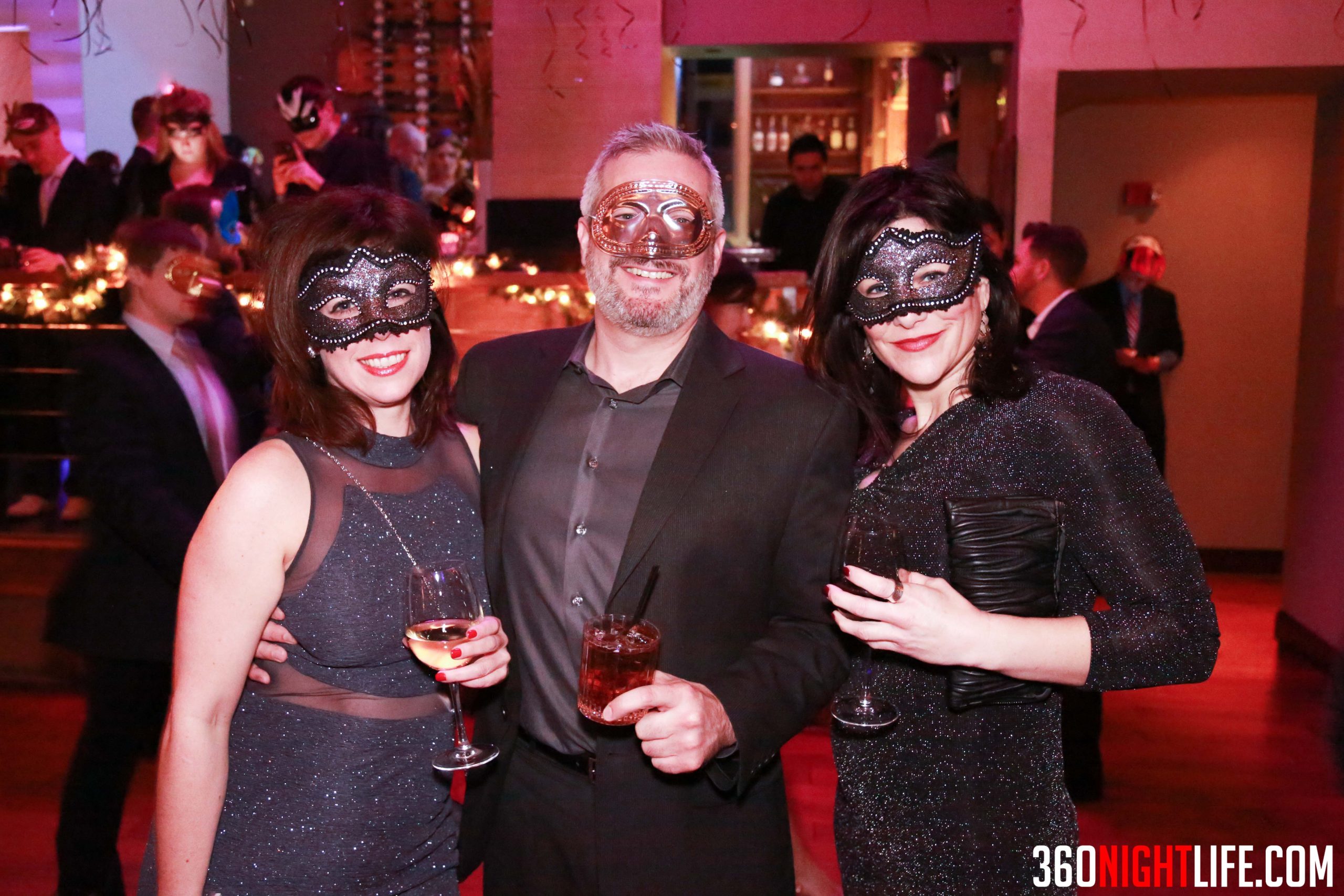 2 women with black masquerade masks on with a man with a grey beard in the middle, he also has a masquerade mask but it is purple or so. They are at the National New Years Eve Masquerade Gala in Washington DC. A very famous and well attended event by 360 Nightlife.